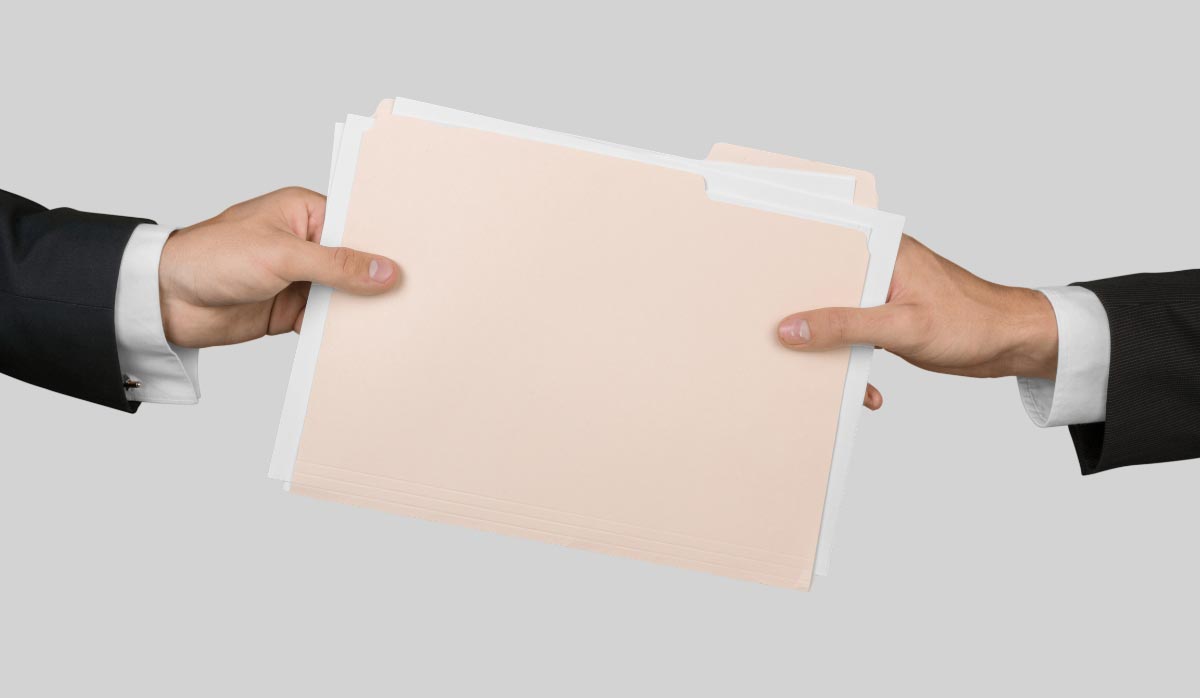 Two people exchanging a folder that represents final closeout documents and project records.