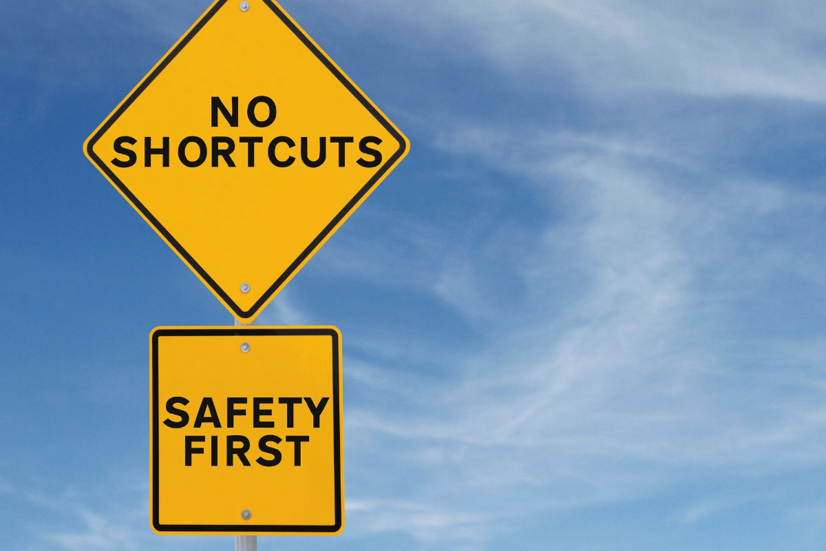 Yellow street sign with the words No Shortcuts and Safety First against a blue sky.