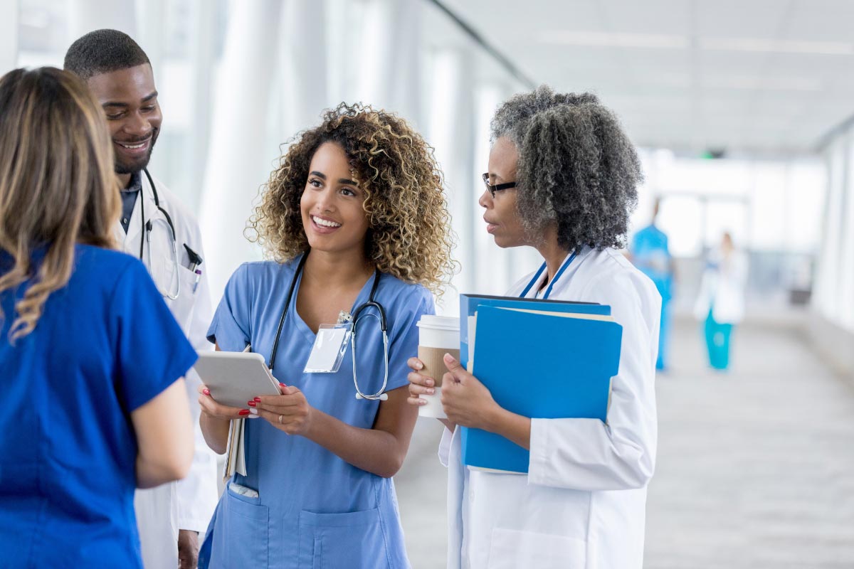 Group of healthcare professionals in a clinic hallway reviewing information on a tablet and paper documents.