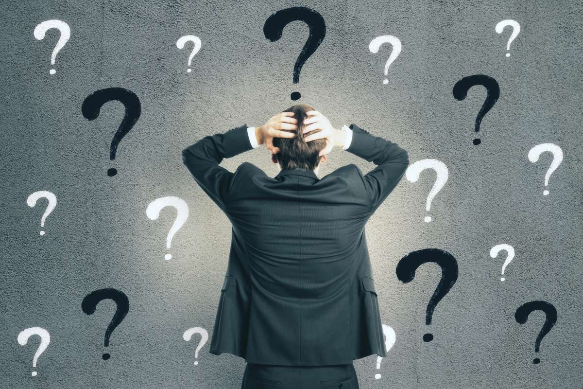 Businessman holding head in frustration surrounded by question marks on wall