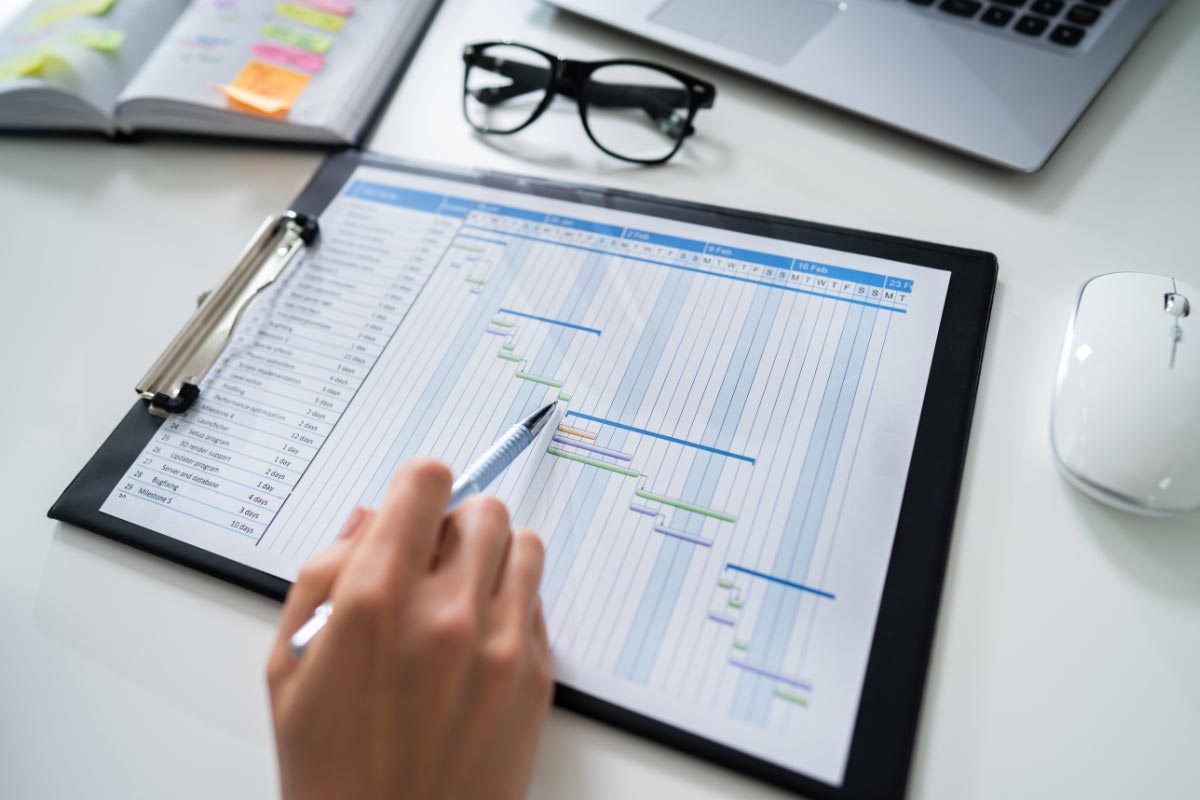 A person pointing to a professional project management Gantt chart on a clipboard, outlining a phased IT rollout schedule.