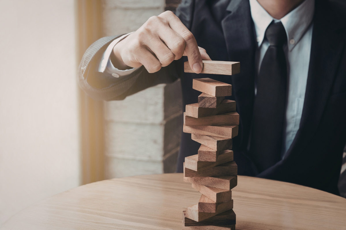 Businessperson stacking wooden blocks symbolizing security risk and infrastructure stability during multi-location expansion.