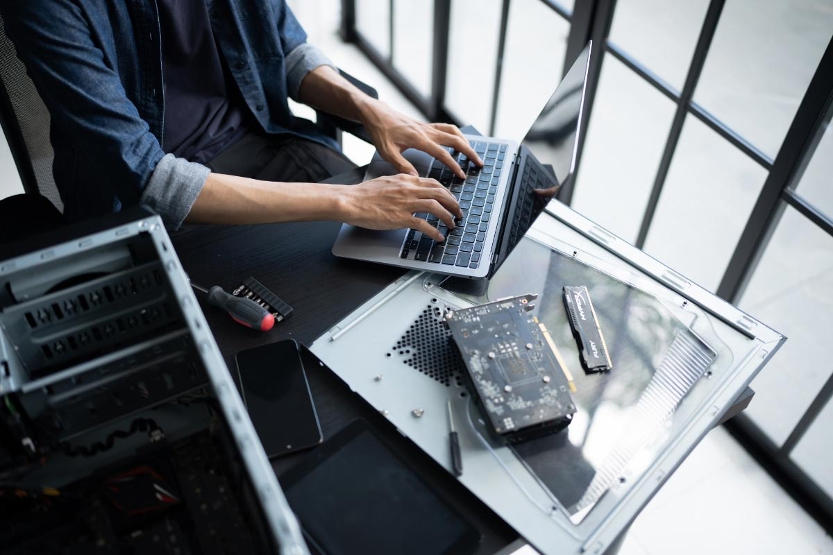 An IT professional at a desk with a laptop and open computer hardware, representing the technical precision required for standardized multi-location rollouts.